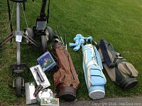 View of two golf push carts, three golf bags with clubs inside, and golf accessories including a monogrammed ball and packaged items