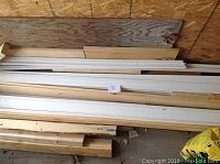 Photo showing multiple 8-foot long white painted trim and baseboard wood pieces stacked horizontally.
