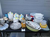 Photo showing the entire assortment of items on a black table including casserole dishes, canisters, silver plated trays, electric knife, and more.