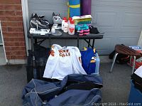 Overview of sports gear laid out on table and floor including skates, water bottles, jerseys, yoga mats, weights and bats.