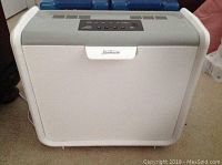 Front view of white Sunbeam humidifier with control panel and power plug visible, placed on floor.
