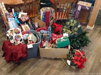 Wide view of entire Christmas lot showing wrapping paper rolls in box, assorted garlands, bows, wreaths, artificial tree parts, and totes filled with textiles and other decorations.