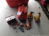 Overview photo showing all items in the lot: battery charger, gas can, jack stands, and tie downs.