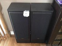 Pair of black floor-standing Fisher 3-way speakers with fabric grills visible from front, placed side by side on wooden floor.