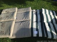 Four chair cushions displayed on grass, showing two matching pairs with different reversible fabrics - floral beige and striped green/beige.