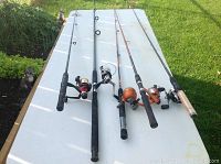 View of five fishing rods with reels laid out on a table showing varied handle types and overall lengths