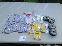 Full lot view showing all fishing lures, rigs, and Sabiki line spools displayed on white table outdoors.