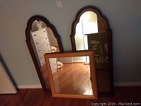 Three wall mirrors shown together leaning on a wall: two matching dark wood arched Top Thomasville mirrors and one square Ikea mirror with a lighter frame in front.