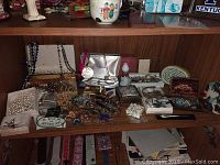 Wide view of shelf showing numerous costume jewelry pieces including necklaces, pins, earrings, bracelets, and trinket boxes.