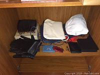 Multiple purses, gloves, and small bags arranged on wooden shelf, including black gloves and various colored purses