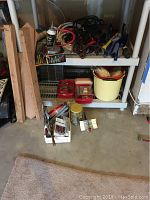 Overall view of shelving unit holding automotive supplies including jumper cables, oil cans, buckets, and assorted small containers and tools.