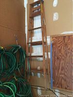 Photo of a 6-foot wooden step ladder leaning against a wall with hose reels nearby.
