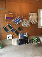 Variety of folding aluminum beach chairs with woven fabric webbing in different styles and colors mounted on wall along with seat cushions on floor below.