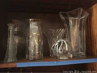 Shelf with a variety of clear glass vases including textured and smooth designs, showing part of the collection.