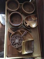 Top view of drawer containing multiple round wooden bowls, leaf-shaped bowl, segmented tray, decorative trivet, and square dish