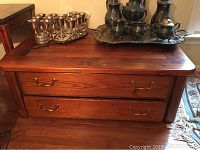 Front view of the wooden coffee table with two brass-handled drawers and displayed silver tea set on top.