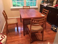 Four wooden Scan chairs surrounding a rectangular wooden table on hardwood floor near window.
