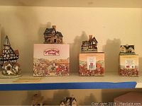 Four miniature David Winter cottages displayed on a shelf, including two cottages shown with original boxes labeled 'David Winter Cottages'