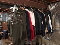 Men's outerwear and shirts hanging on a metal rack in a basement or storage setting. Various colors and styles visible.