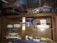 Kitchen cabinet with stacked Corning Ware ceramic bakeware and plastic storage containers and serving bowls