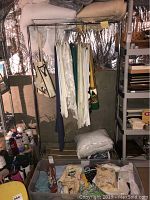 Photo of linens hanging on metal rack including table cloths, oven mitts, and blankets. Boxes and folded linens visible below rack.