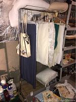 Front view of metal clothes rack with skirts and bags hanging, showing support structure and background items.