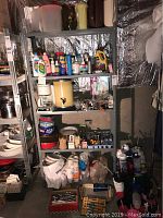 Shelving unit with water pitchers, household chemicals, coffee makers, baking tins, flatware, and various household products.