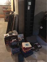 Full view of the lot showing stacked folding tables, boxes containing toys, games, cassette tapes, and tall black cassette tower