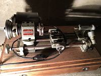 Overall view of lathe assembly showing headstock, motor, belt-driven pulleys, twin-bed rails, carriage and tailstock on wooden base.