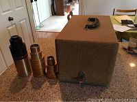 Three gold projector lenses and vintage Golde slide projector carrying case on a countertop.