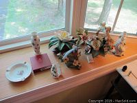 Wide view of all items including porcelain flowers, vase, bird figurine, ashtray, and boxed coasters arranged on a window sill.