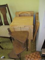 Wooden TV trays stacked together against the wall alongside the corner stand and luggage rack visible beside wooden chairs.