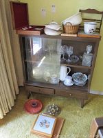Wooden display cabinet holding various glassware, pottery bowls, planters, and tea cups with floral patterns.