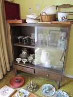 Front view of wooden cabinet with sliding glass doors showing glassware and dinnerware inside and items on top