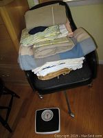 Folded assorted linens and towels stacked on a black chair, bathroom scale on floor in front