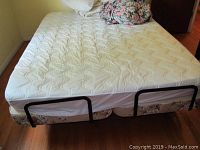 Top view of queen size mattress and adjustable bed frame with floral box spring beneath and side rail attached.