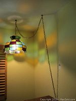 Hanging colorful stained glass pendant lamp suspended by a metal chain, casting multi-colored light reflections on the wall.