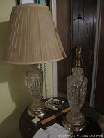 Two glass base lamps side by side; one with beige pleated shade, one missing shade