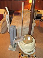Oreck Classic XL upright vacuum cleaner and Bissell Carpet Machine Plus placed next to a beige couch and other household furniture, showing overall condition and size of vacuums.