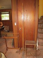 Photo showing wood quilt rack, wood coat rack, small metal table, and metal magazine rack placed against a wooden wall and carpeted floor.
