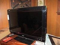 Front view of Sharp Aquos 32-inch flat screen television showing the screen and stand along with remote and box beside it.