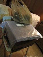 Photo of a silver Panasonic VHS player wrapped in plastic, resting on a green chair with plastic bags on top.