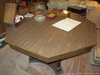 Octagonal wood grain game table shown with playing cards and other game pieces on the surface, alongside ashtrays and an ice bucket.