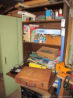 Wood shelving unit filled with various boxes, wood box, tools, and hardware. Moen faucet box visible.