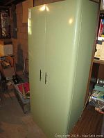 Full front view of the tall pale green metal cabinet with closed doors, showing slight surface wear and scratches.
