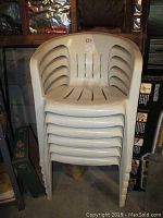 Stack of six white plastic chairs showing front view and armrests.