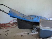 Lawn mower with Dust Blocker bag, gas can partially in view, and blue tarp draped over mower.