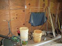 Photo showing Greenfield spreader, plastic buckets, lawn sweeper, and two snow shovels leaning in wooden shed