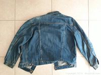 Back view of medium blue denim jacket with long sleeves and side hem tabs.