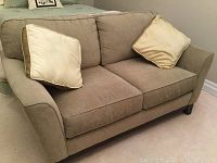Photo of beige upholstered love seat with two seat cushions, two back cushions, and two decorative beige cushions included
